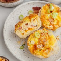 An overhead view of three mini quiches on a speckled white plate. One quiche is laying on it's side with a bite missing.