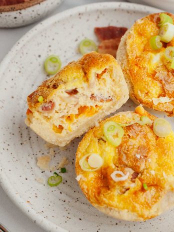 An overhead view of three mini quiches on a speckled white plate. One quiche is laying on it's side with a bite missing.