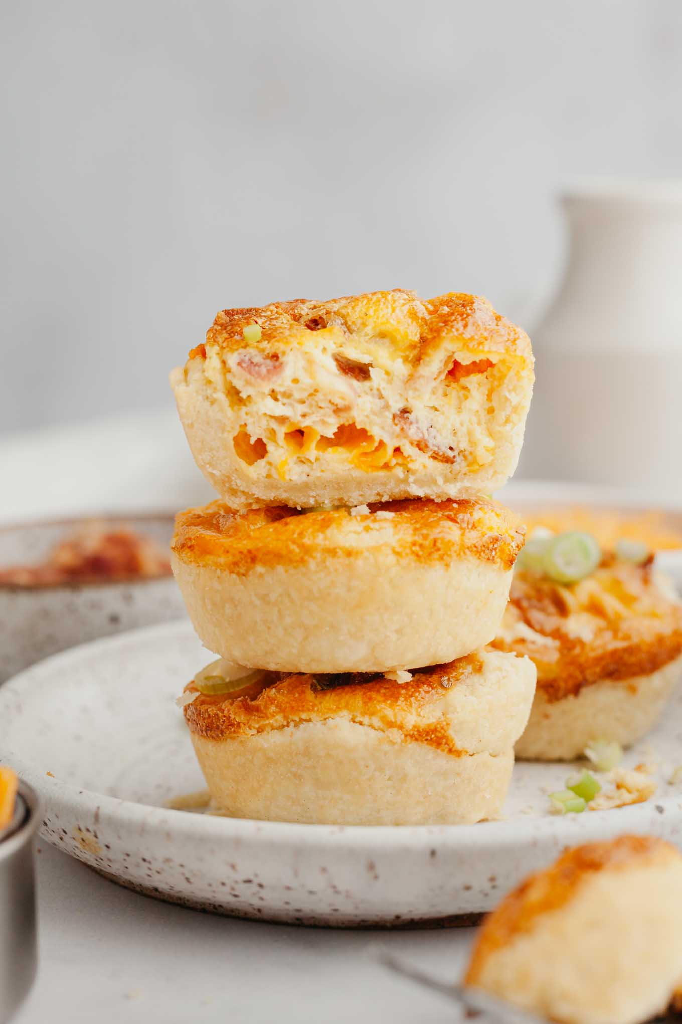 A stack of three bite-sized quiche on a speckled white plate. 