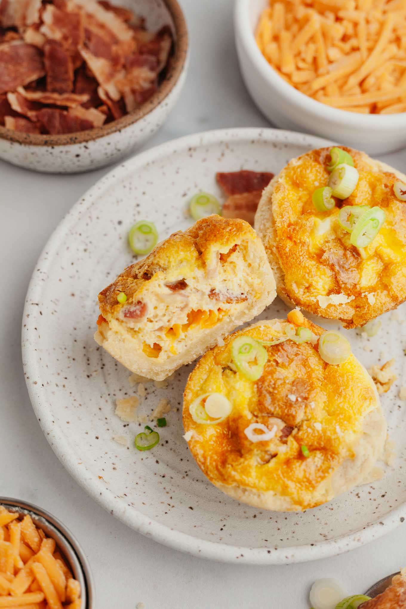 An overhead view of mini quiches on a plate. One quiche has been cut in half. 