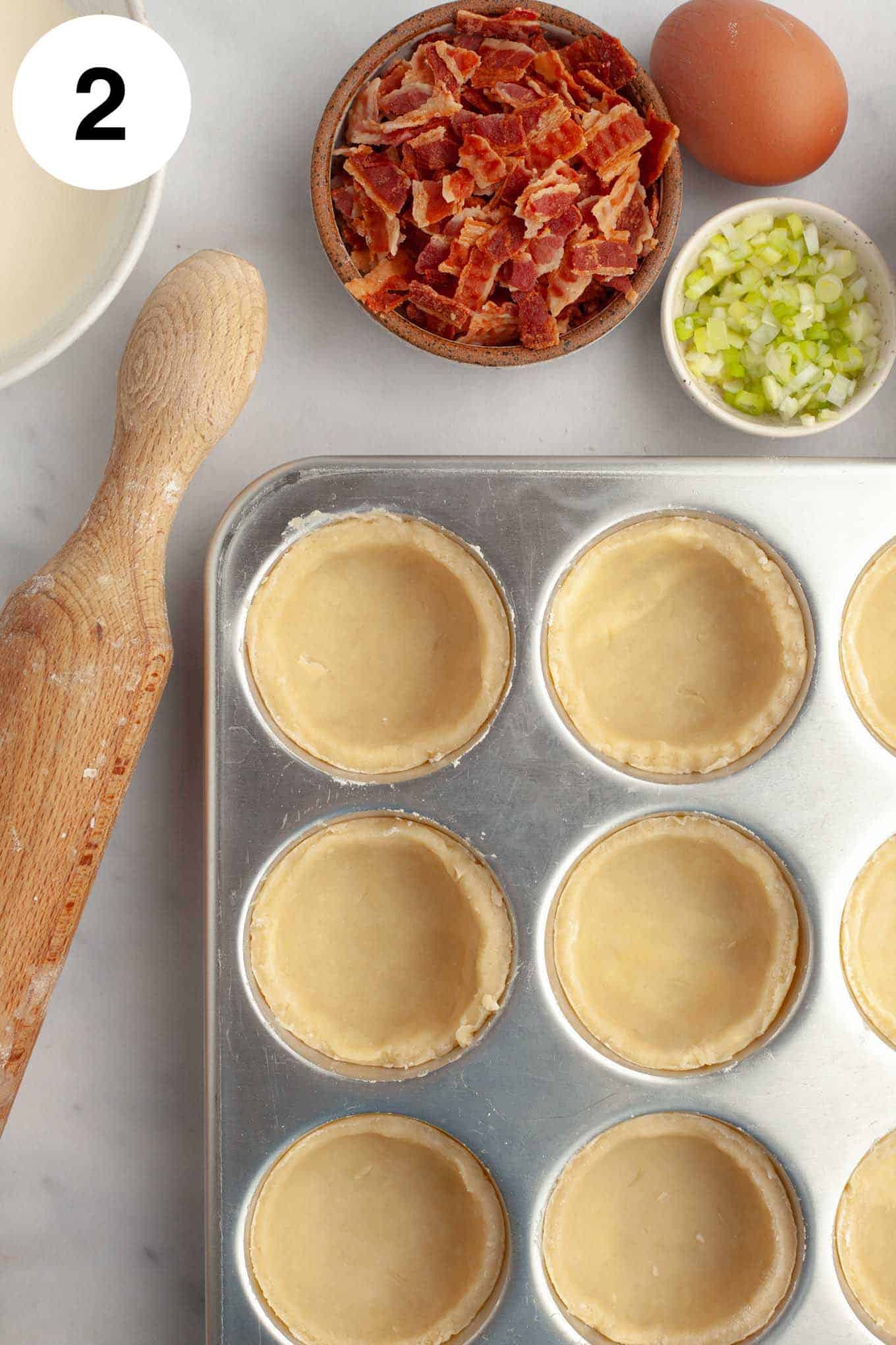 An overhead view of mini quiche crusts pressed into muffin cups. 