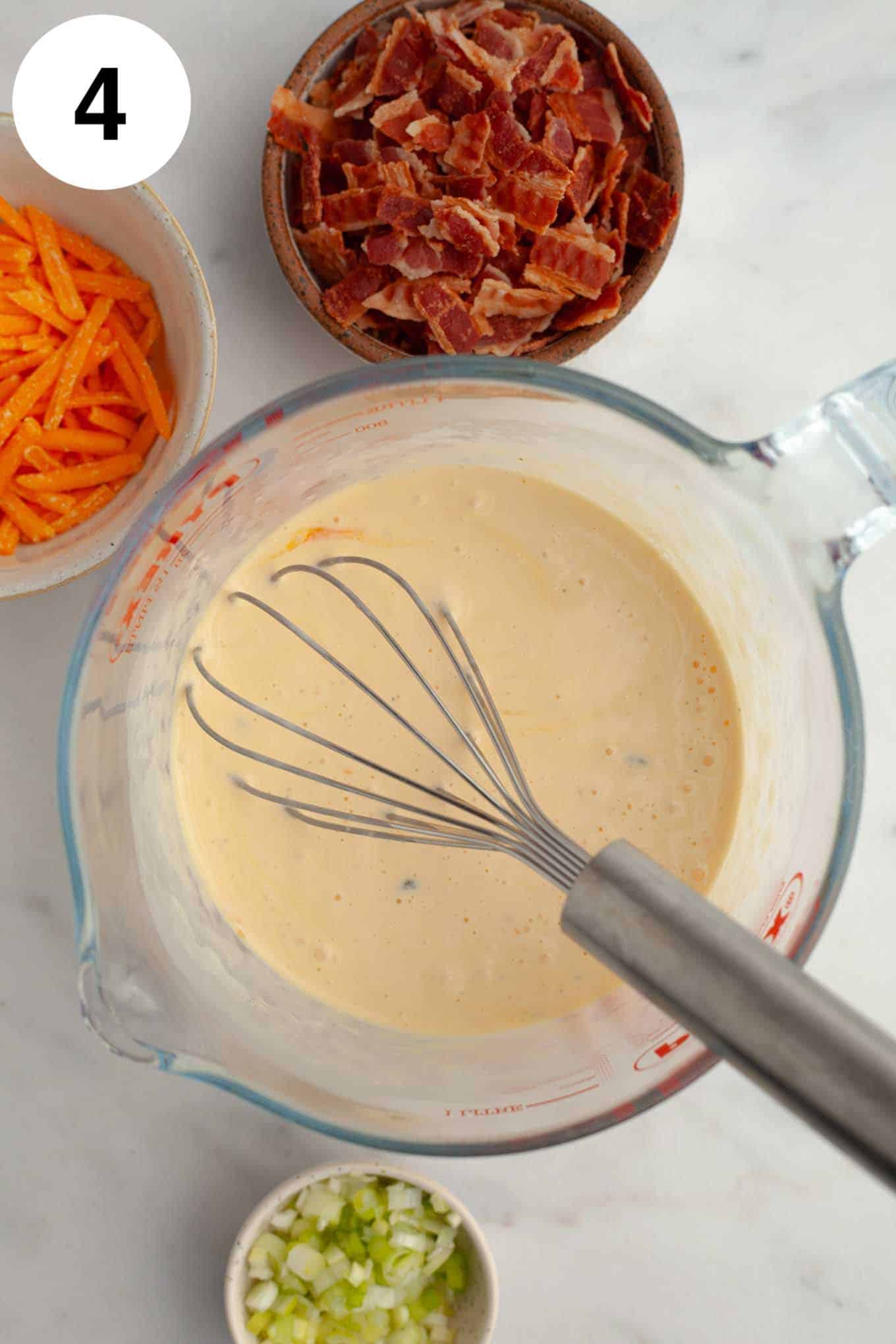 An overhead view of mini quiche filling in a glass measuring cup. 