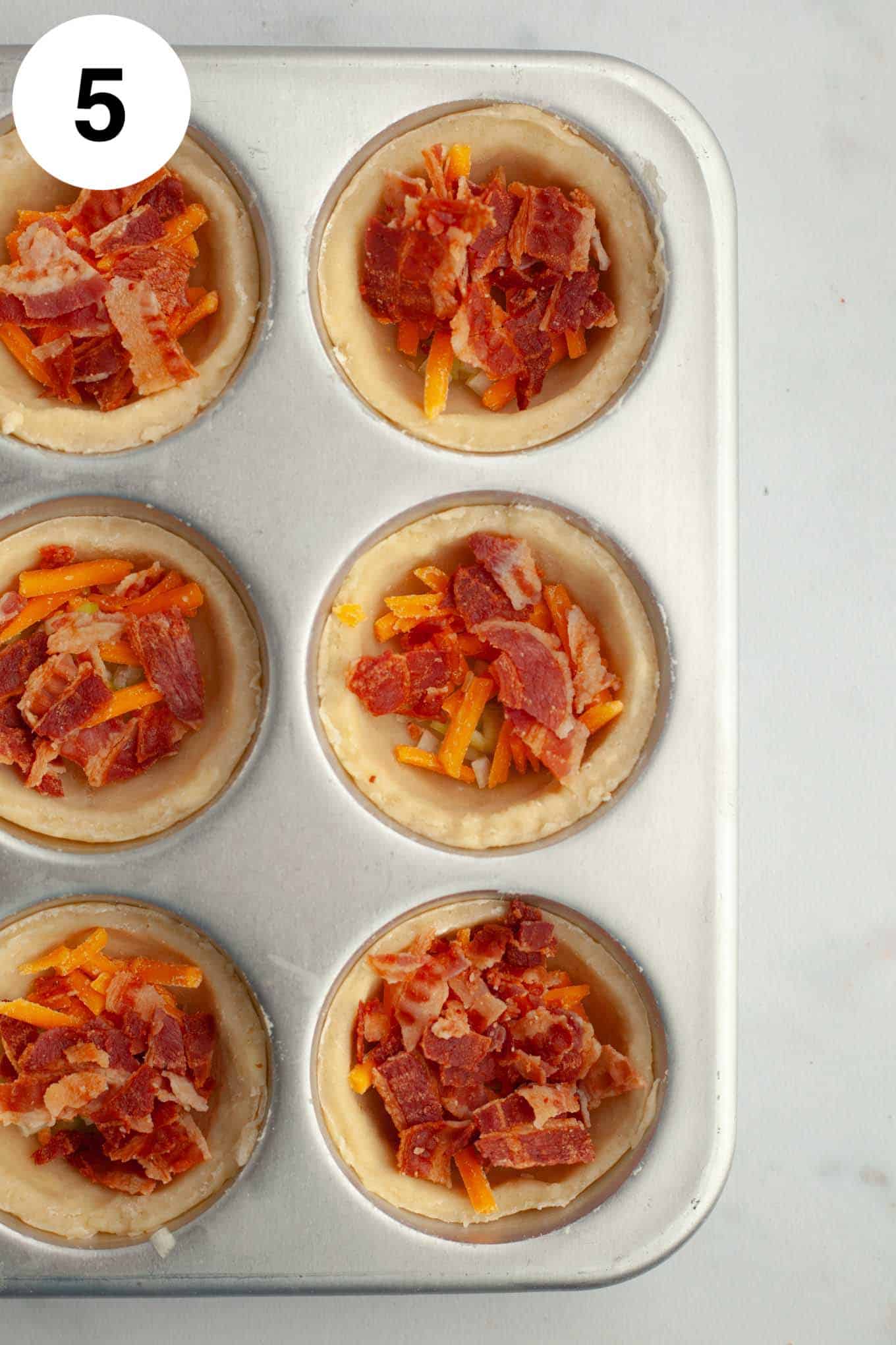 An overhead view of partially filled mini quiches in a muffin pan. 