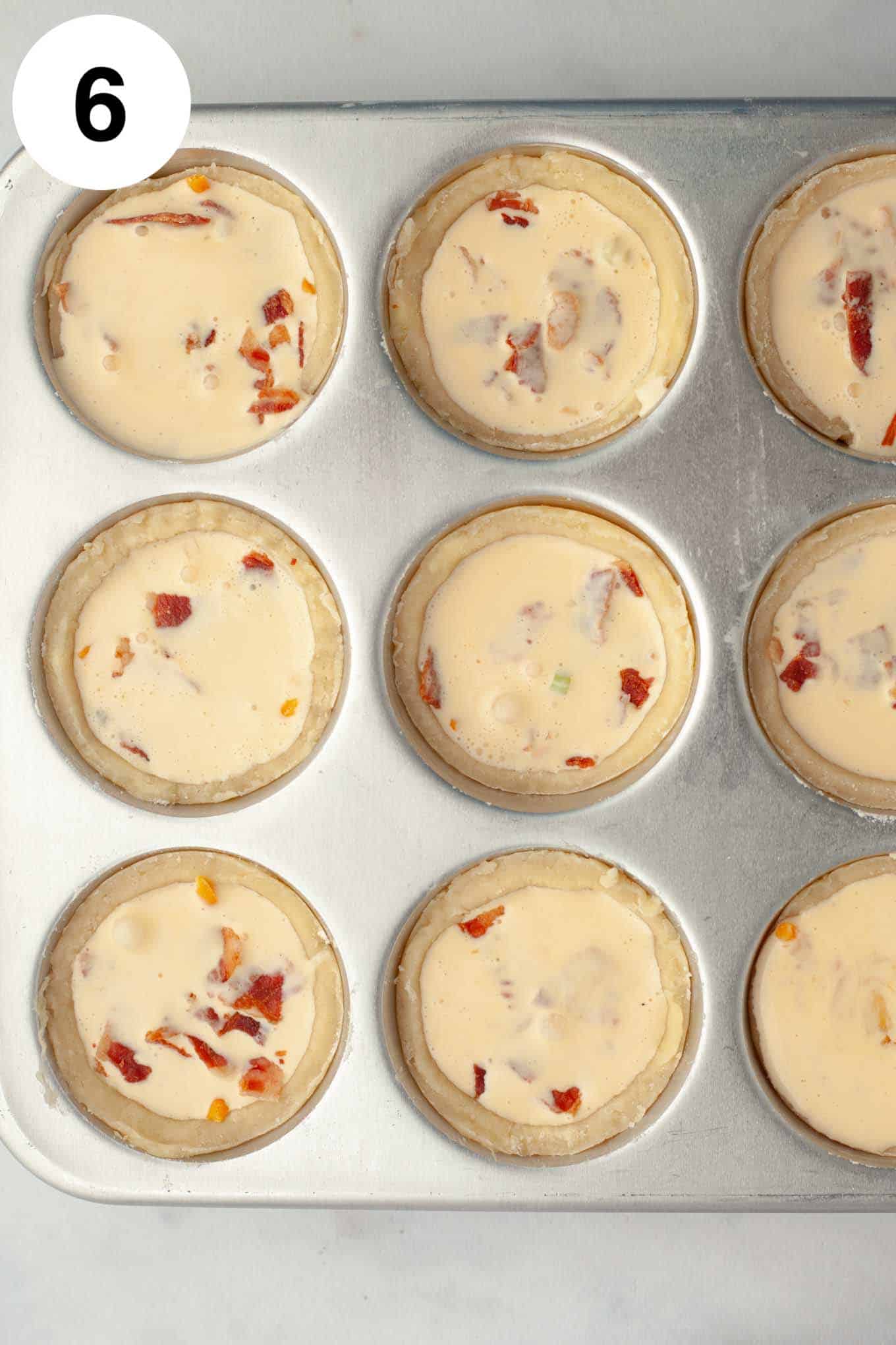 An overhead view of unbaked, filled mini quiches in a muffin pan. 