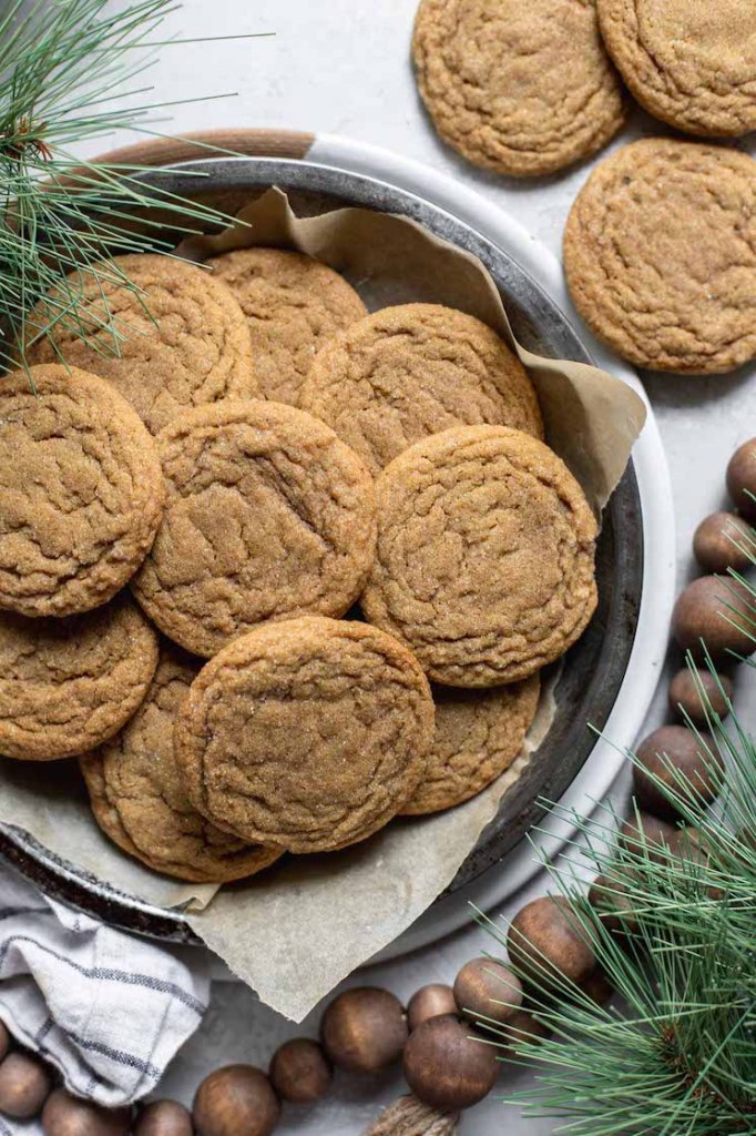 A round baking pan filled with molasses cookies surrounded by rustic Christmas decorations.