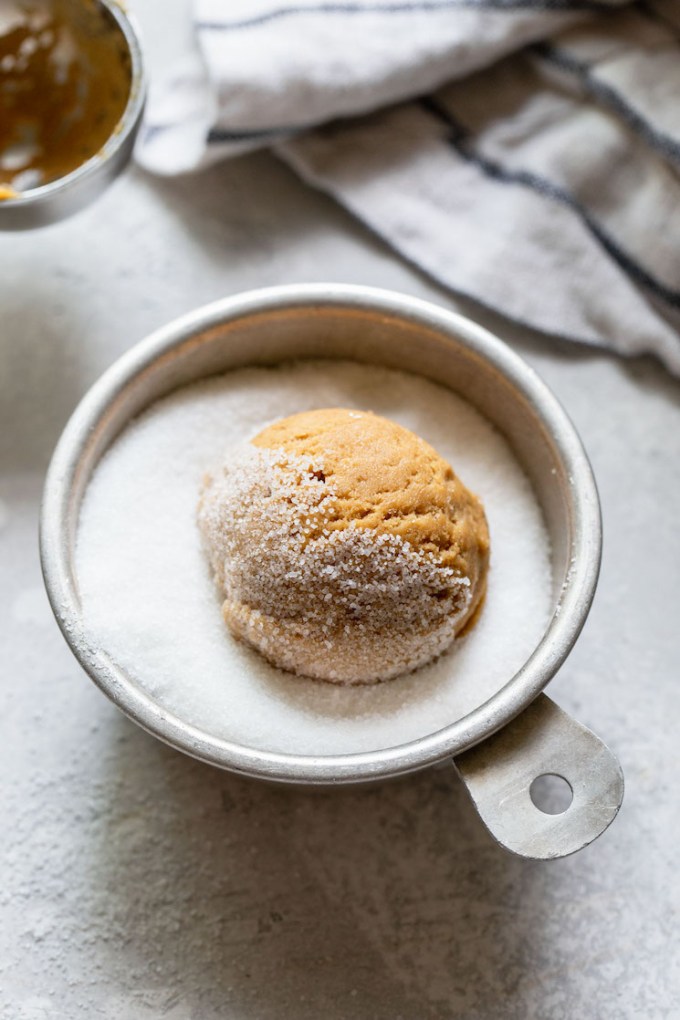 A ball of cookie dough being rolled in granulated sugar.