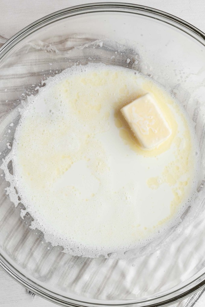 Overhead view of sugar, butter, salt, and scalded milk in a large mixing bowl.