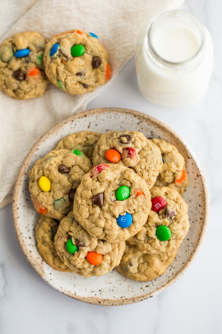 Monster cookies on a plate with more cookies and milk on the side.