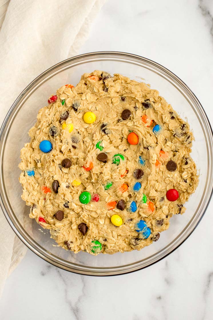 A glass bowl filled with monster cookie dough on top of a marble surface.