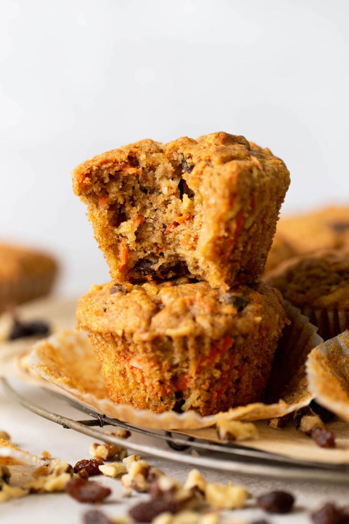 Two morning glory muffins stacked on top of each other, on a wire rack. The top muffin has a big bite missing. 