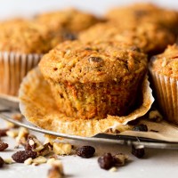 Side view of morning glory muffins on a wire cooling rack. The front muffin has had the paper liner pulled down.