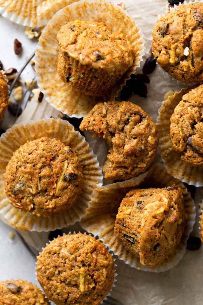 Overhead view of morning glory muffins in muffin liners on a wire cooling rack. Some of the muffins are turned on their sides, and one has a bite missing. 