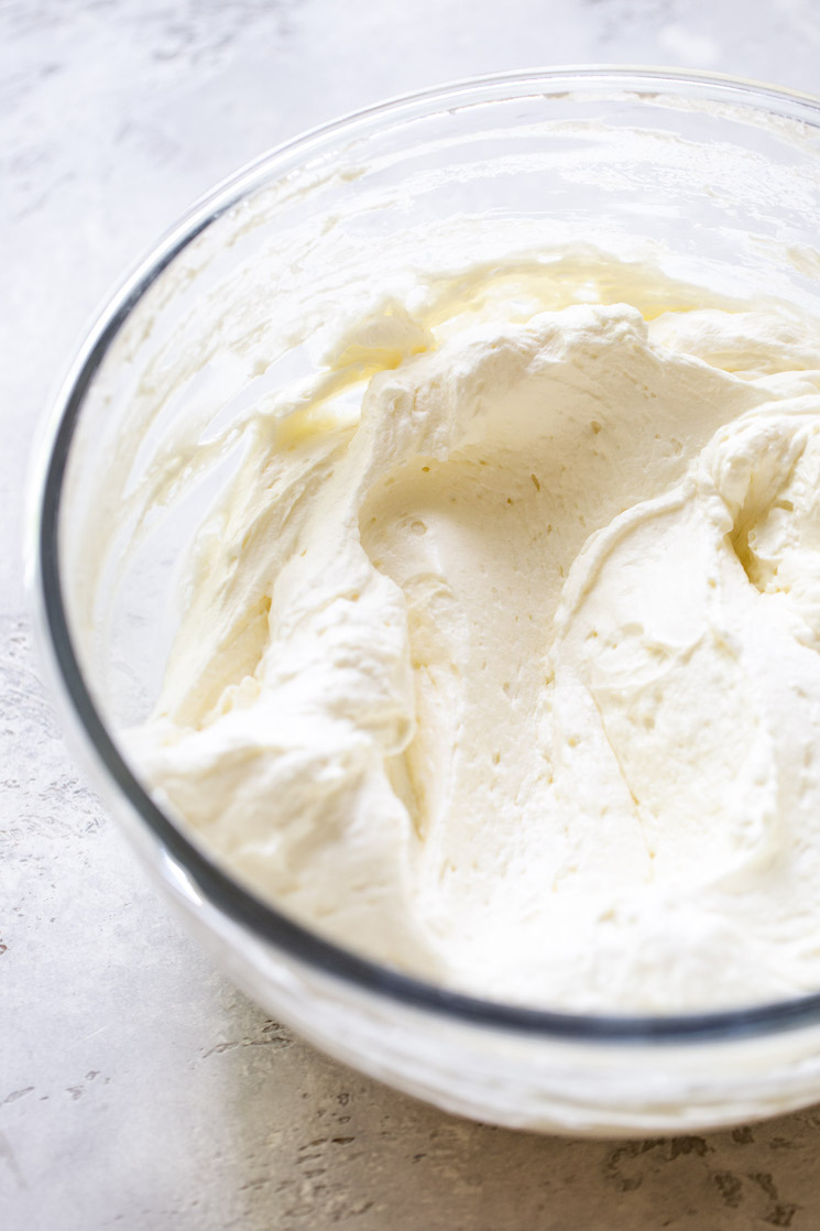 The no-bake cheesecake ingredients mixed up in a glass mixing bowl on top of a rustic gray surface. 