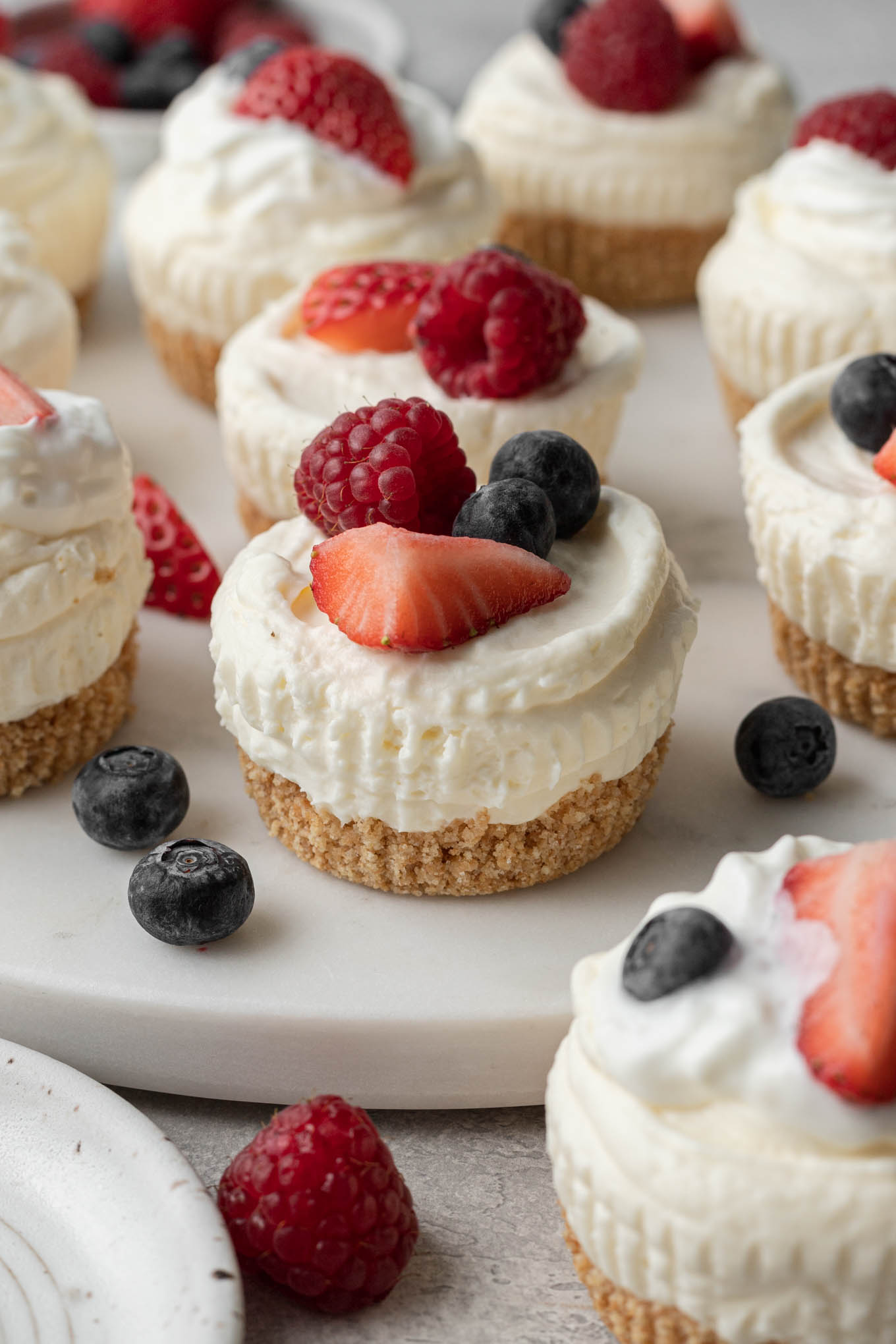 Mini no-bake cheesecakes topped with fresh berries on a white platter. 