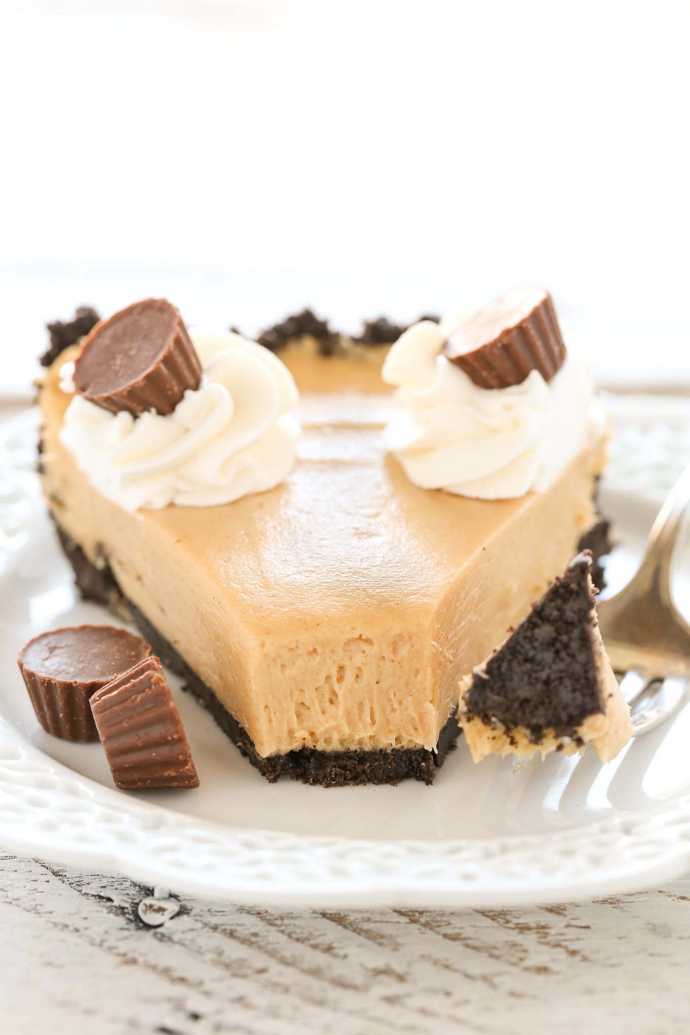 Front view of a slice of oreo peanut butter pie on a white plate with a fork. A bite of pie is missing. 