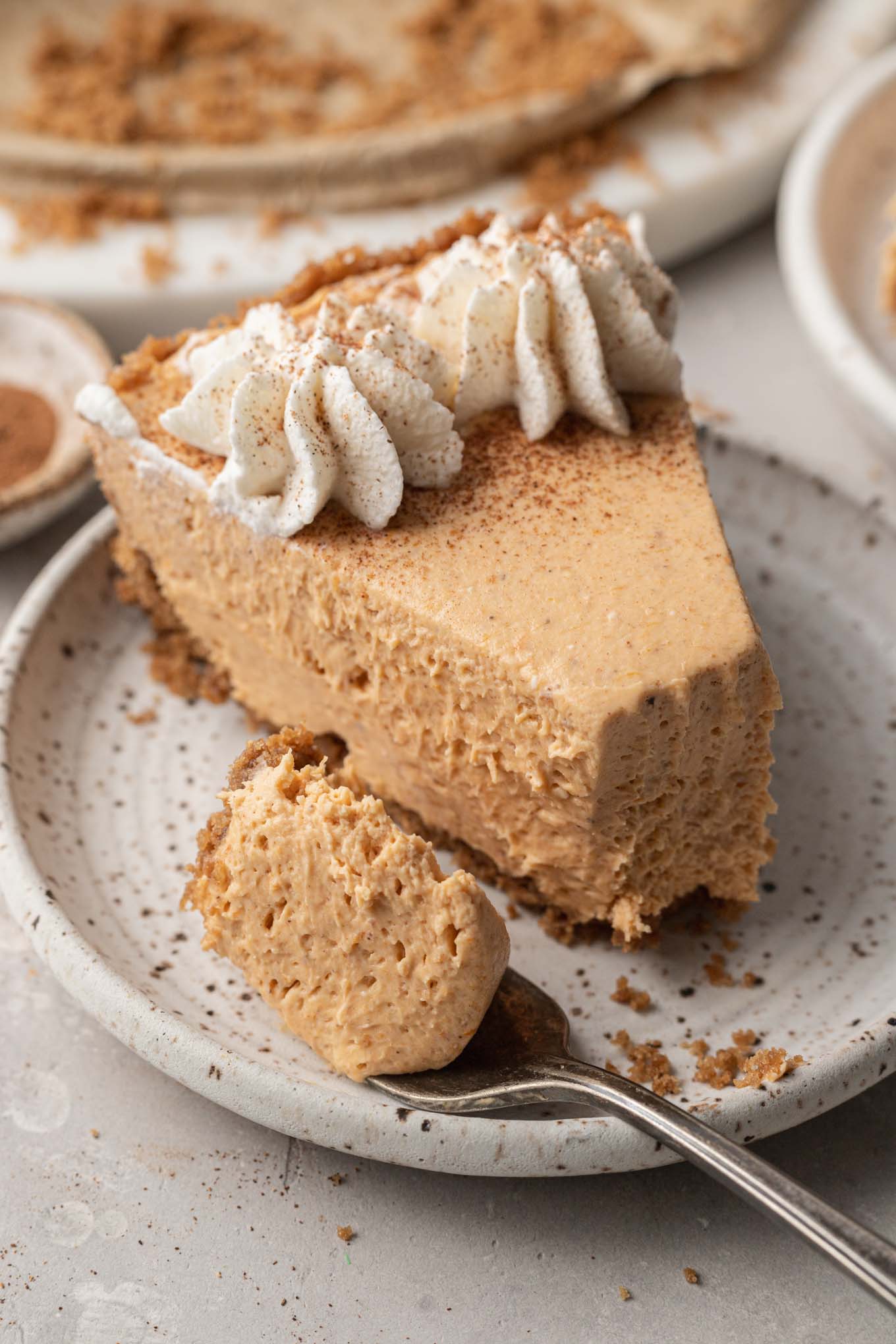 A slice of pumpkin no bake cheesecake on a speckled dessert plate, with a fork on the side. 