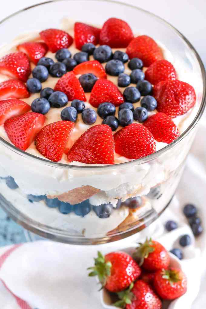 Top view of a berry trifle garnished with fresh strawberries and blueberries. A small dish of strawberries rests in the foreground. 