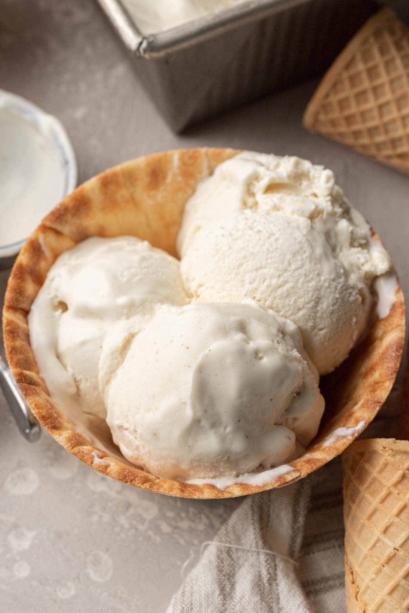 A waffle cone bowl filled with three scoops of vanilla ice cream. 