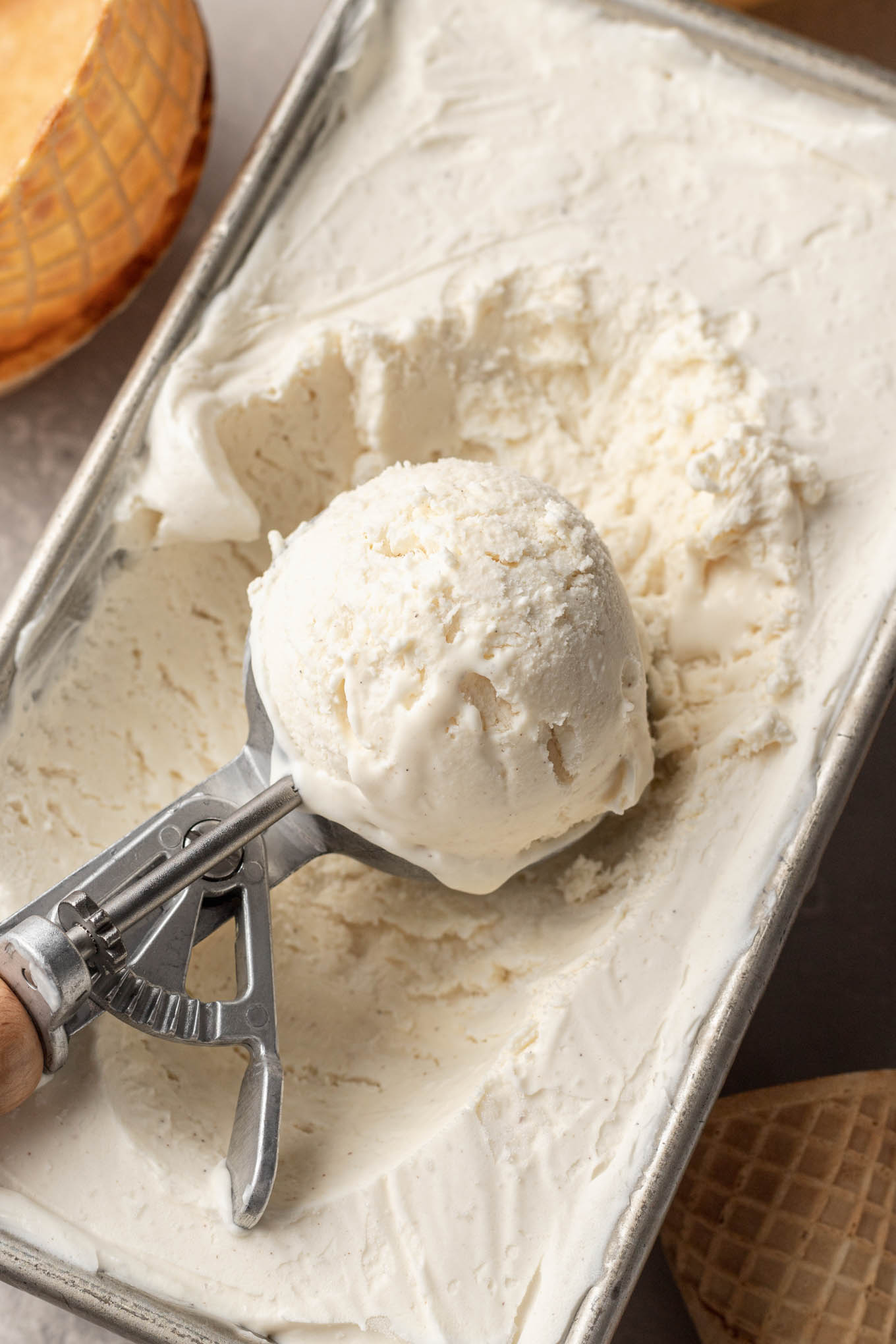 An ice cream scoop resting on top of a pan of no churn homemade ice cream. 