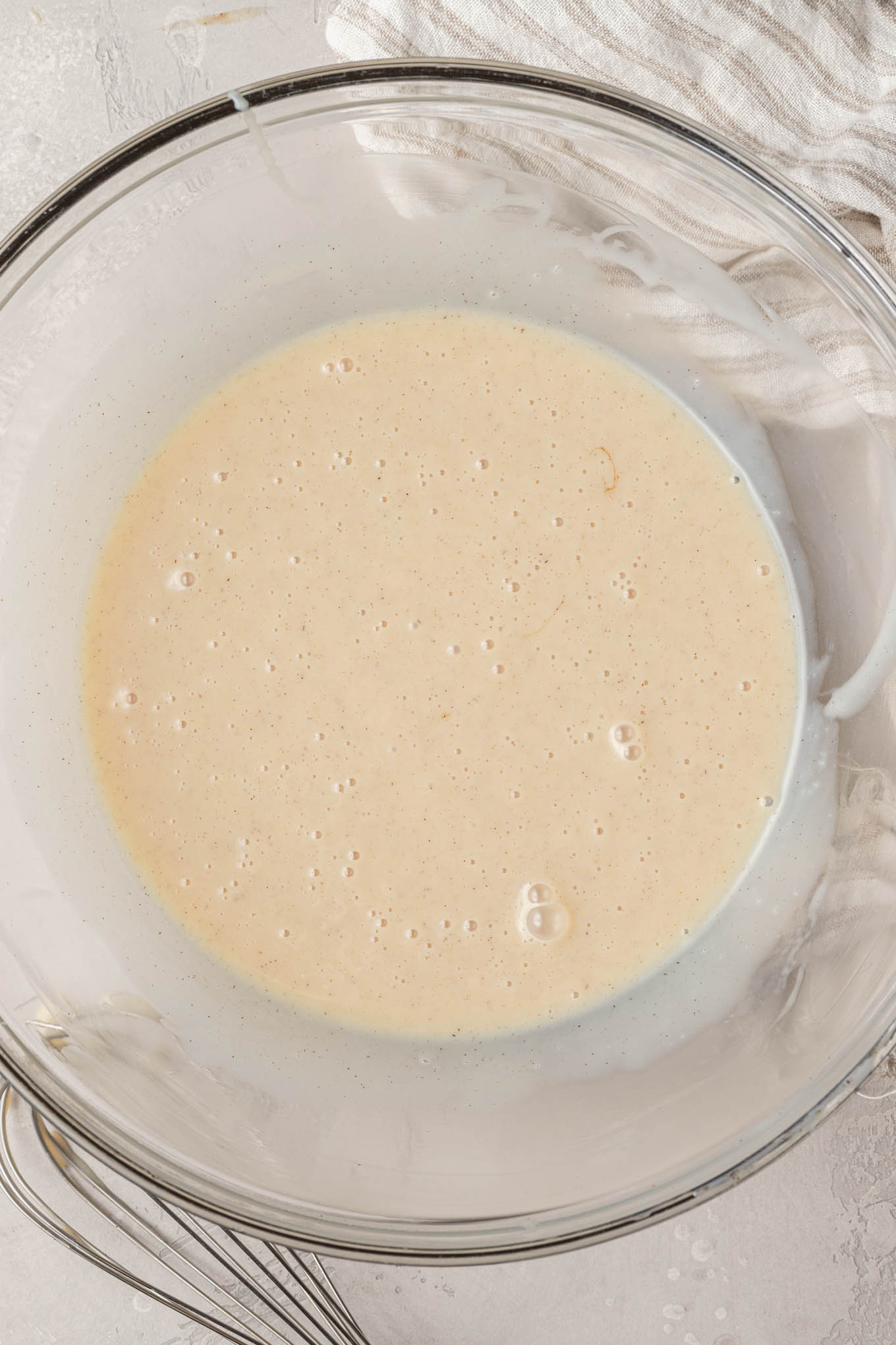 An overhead view of a glass mixing bowl filled with sweetened condensed milk, vanilla, and salt whisked together.