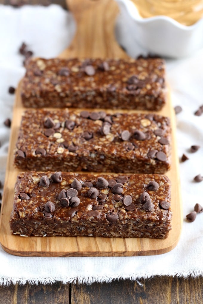 Three homemade chewy chocolate chip granola bars on a wood board. 