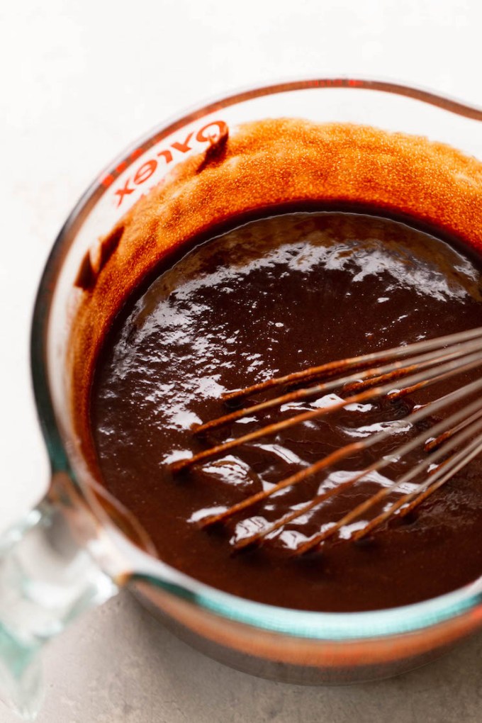 An overhead view of brownie batter in a glass bowl with a whisk.