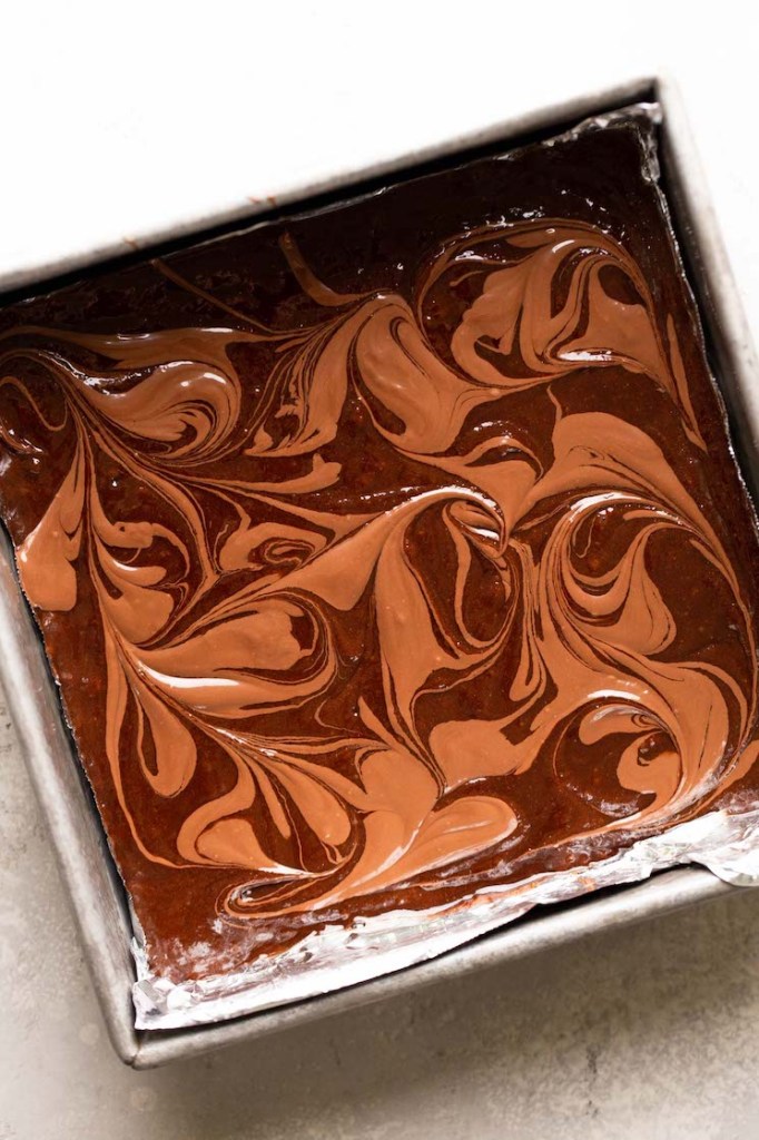 An overhead view of brownie batter that's been swirled with Nutella in a metal baking dish. 