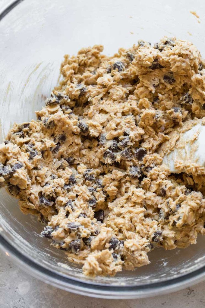 A glass mixing bowl filled with oatmeal chocolate chip cookie dough.