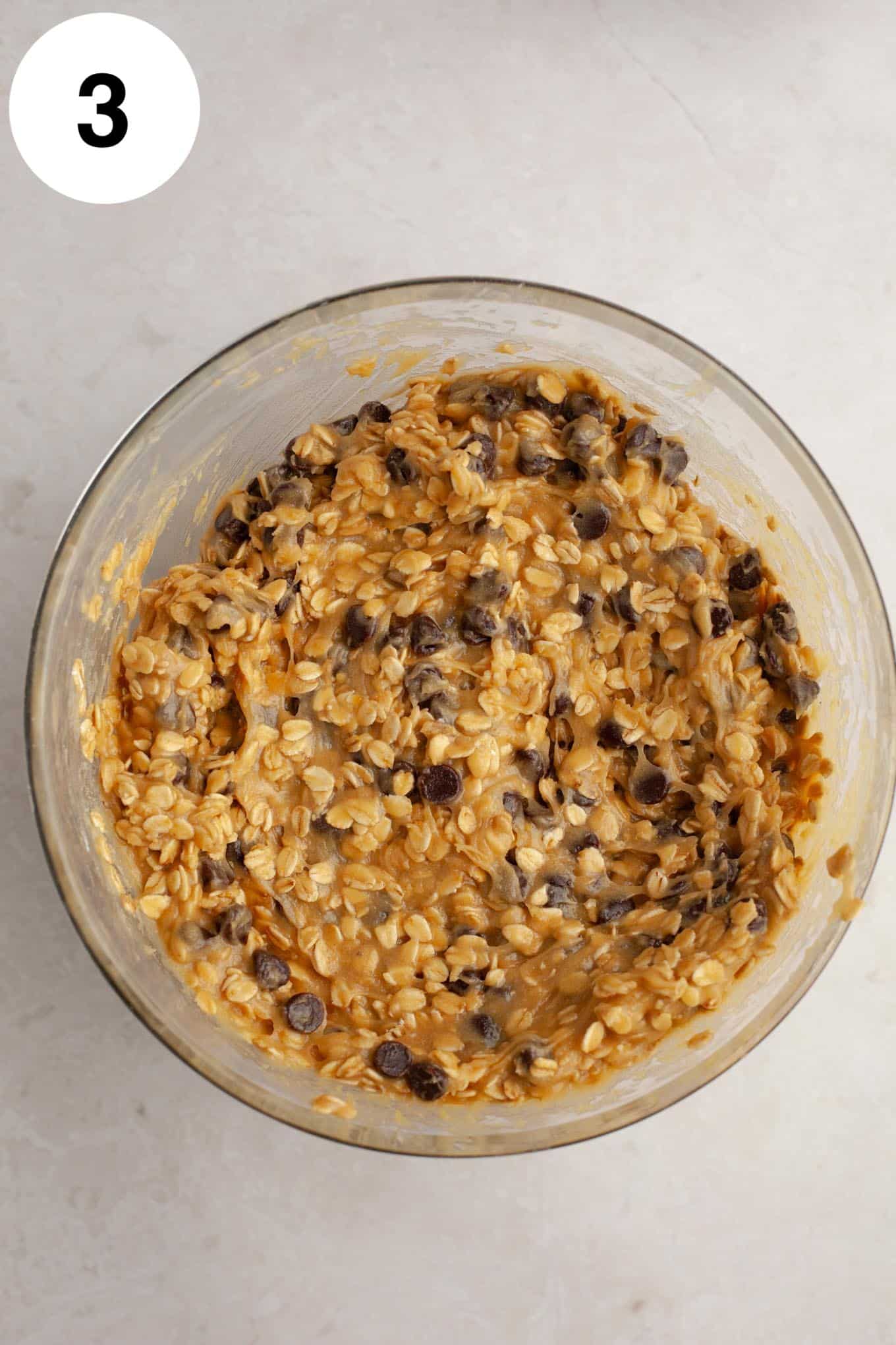 An overhead view of oatmeal chocolate chip cookie dough in a glass mixing bowl.