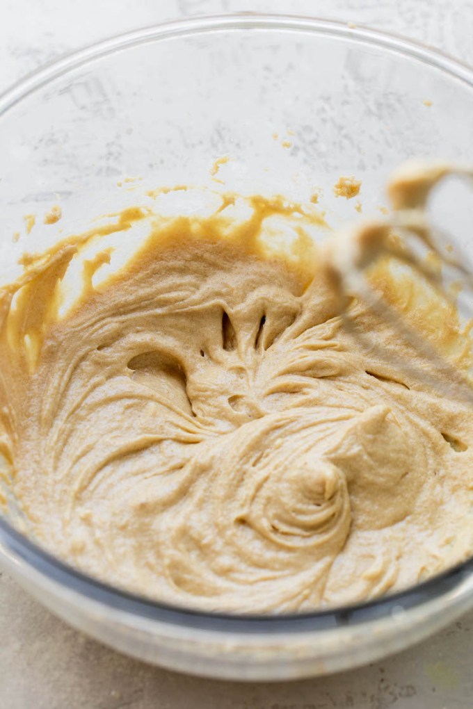 A glass mixing bowl holding the wet ingredients for cookie dough that has been mixed together.