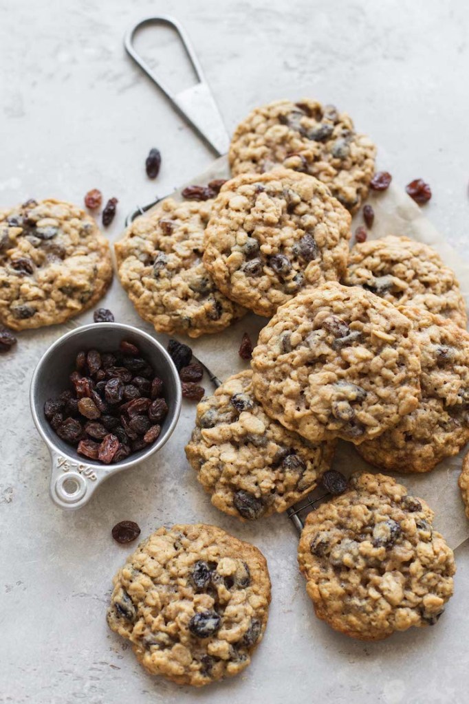 A batch of cookies laid out on top of a small cooling rack with more raisins scattered around them.