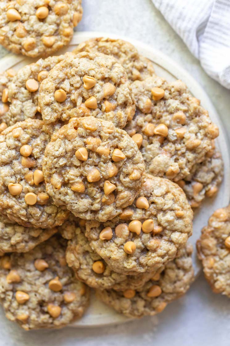 A stack of oatmeal scotchies on a rustic clay plate with a striped napkin in the background. 