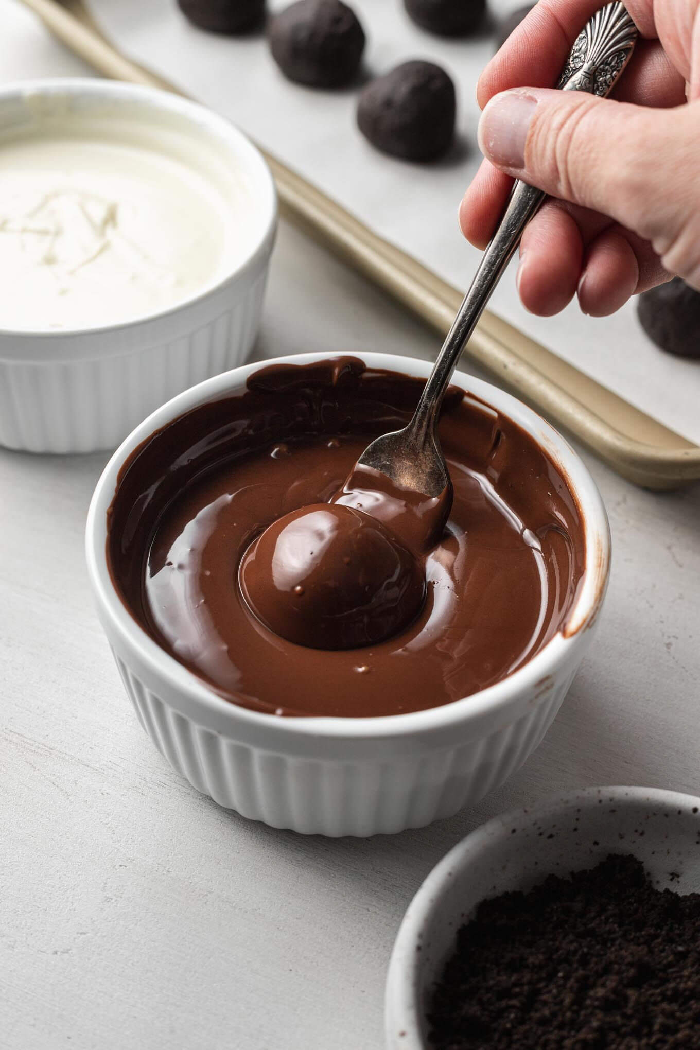 An Oreo ball being dipped into a bowl of melted chocolate. 