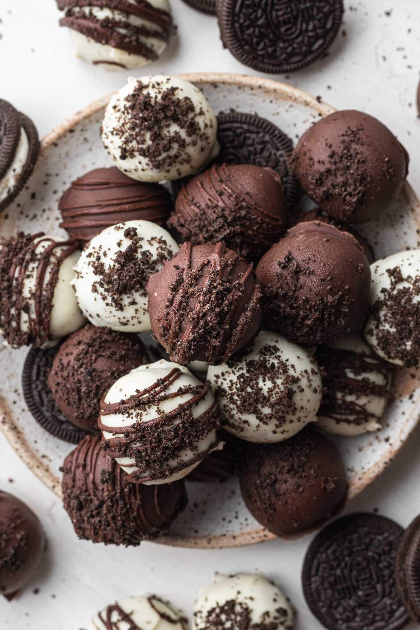 An overhead view of chocolate-dipped Oreo balls piled on a speckled white plate. 