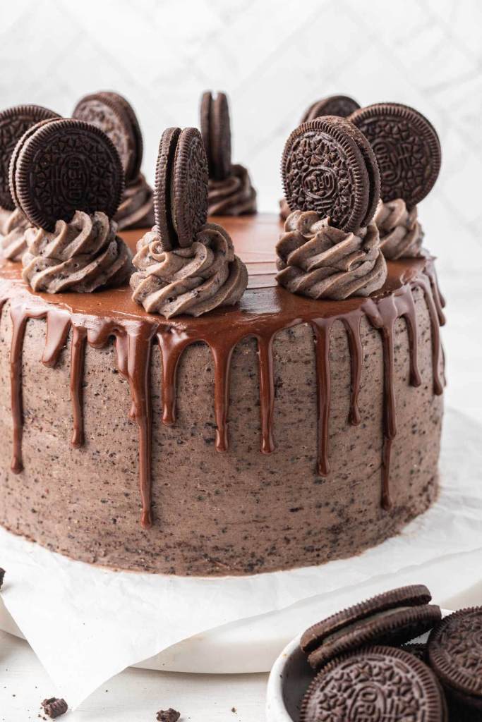 A chocolate Oreo cake, decorated with a chocolate ganache drip, swirls of frosting, and whole Oreos. 