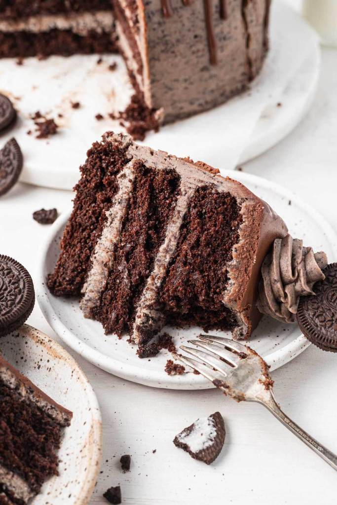 A slice of Oreo cake on a white dessert plate; a bite is missing. 