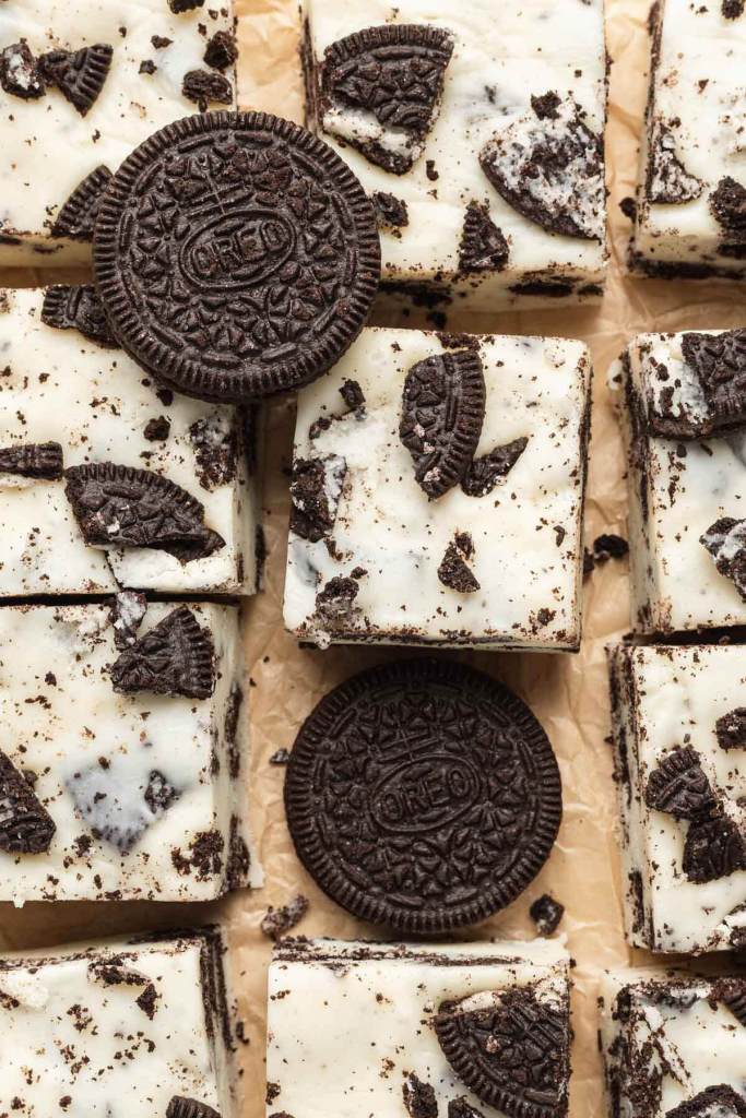 An overhead view of slices of cookies and cream fudge on parchment paper. Two Oreo cookies rest atop the fudge. 