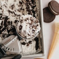 An overhead view of Oreo ice cream in a loaf pan. An ice cream scoop with a scoop of ice cream sits on top of the loaf pan.