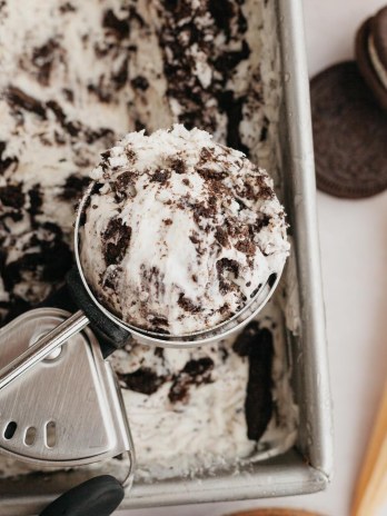 An overhead view of Oreo ice cream in a loaf pan. An ice cream scoop with a scoop of ice cream sits on top of the loaf pan.