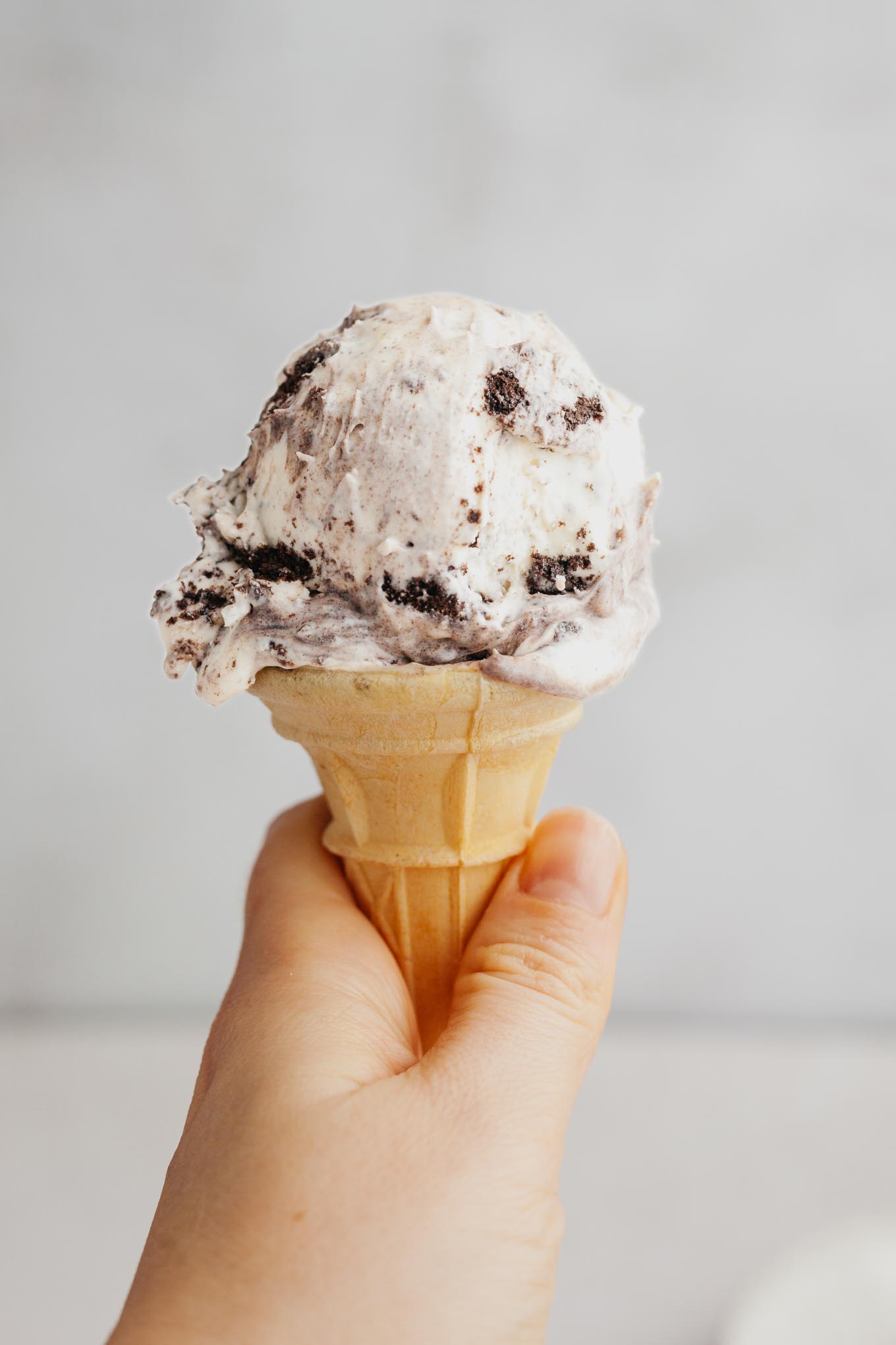 An Oreo ice cream cone being held aloft. 