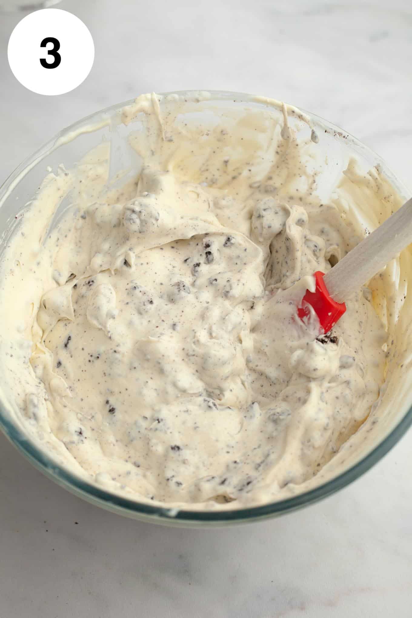 An overhead view of a homemade Oreo ice cream base in a glass mixing bowl. 