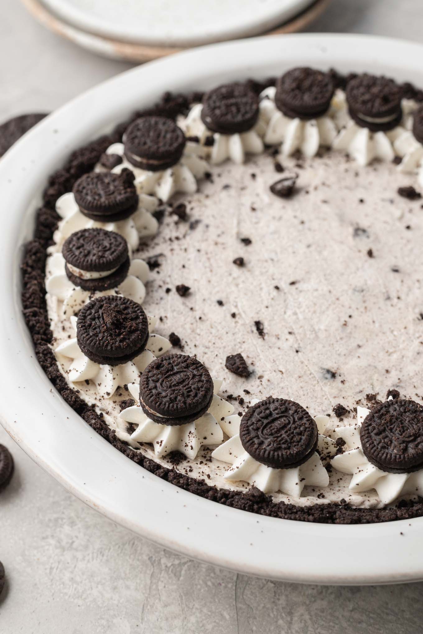 A side view of an Oreo pie with whipped cream piped around the edges and mini Oreos pressed on top of the whipped cream.