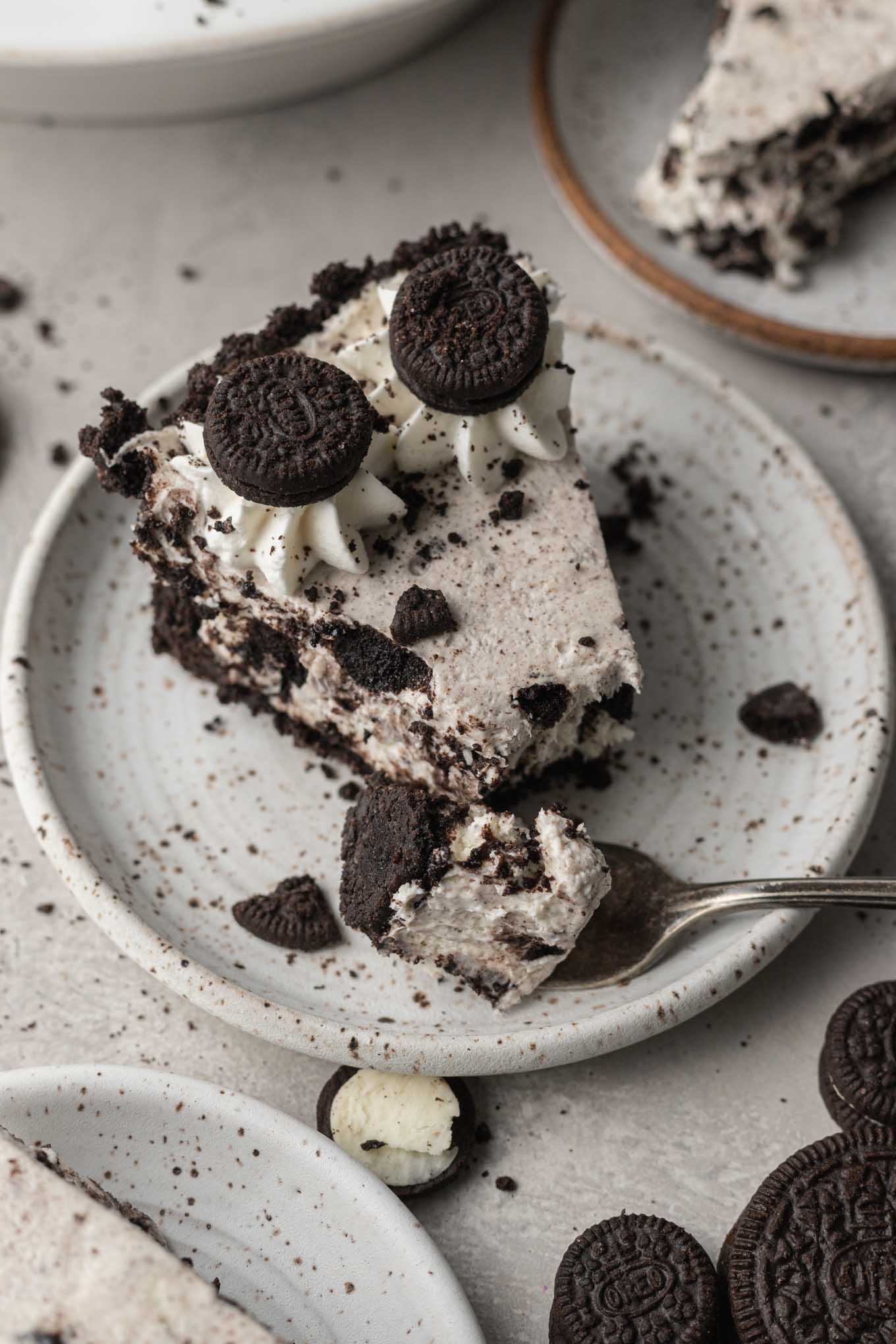 A slice of Oreo pie on a speckled white dessert plate. A piece of the pie has been removed with a fork, which rests on the plate.