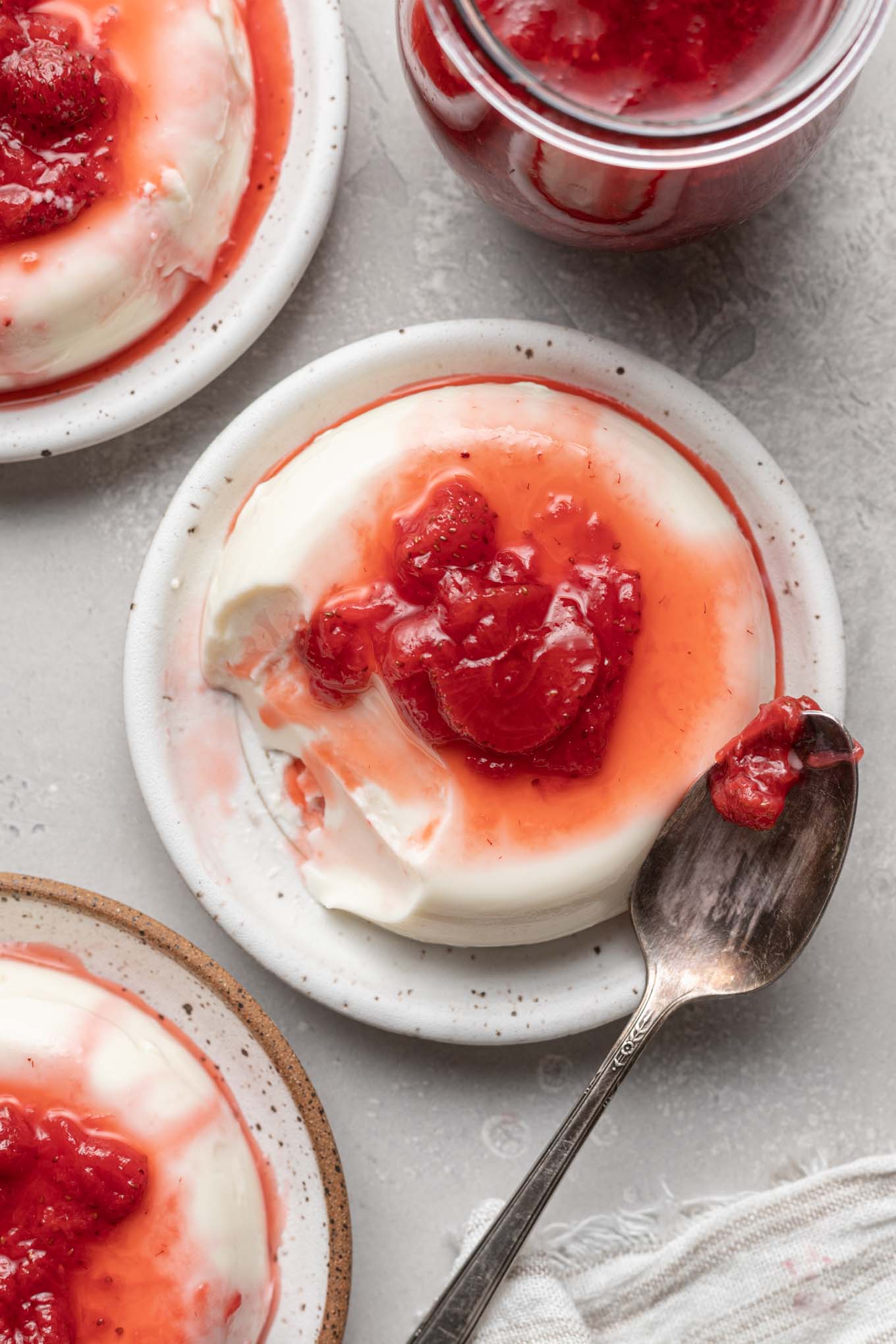 An overhead view of three strawberry panna cotta servings on small plates. 