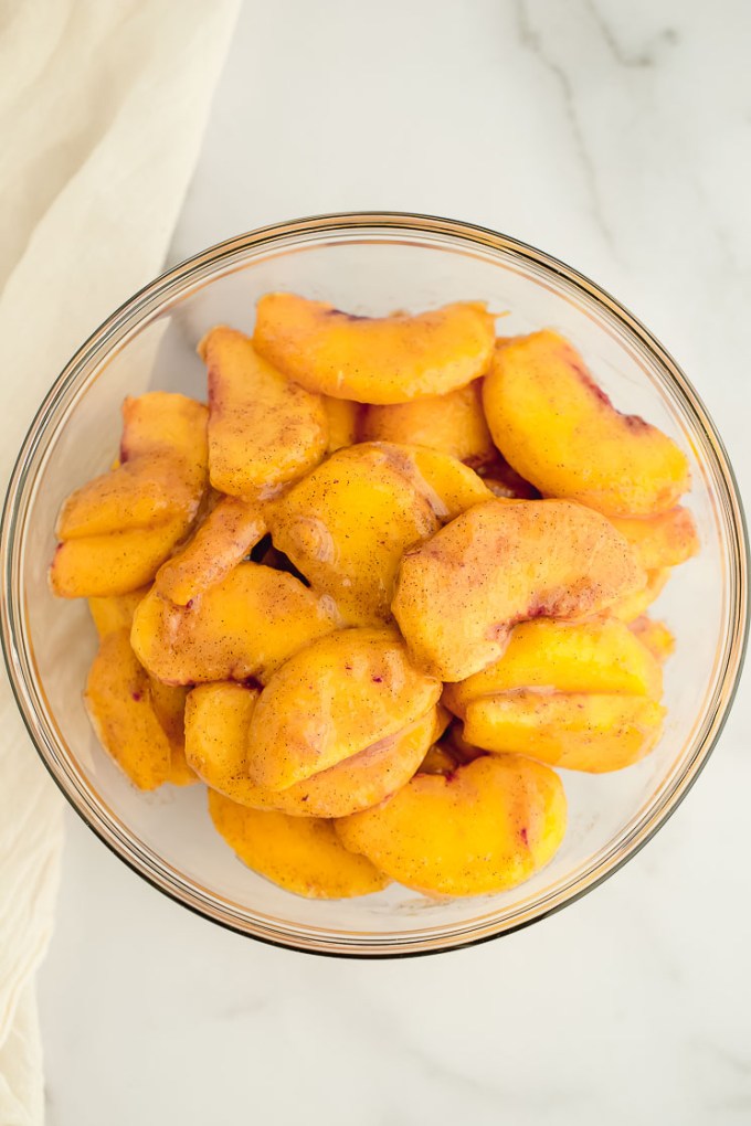 A bowl filled with sliced peaches coated in cinnamon, corn starch, and sugar.