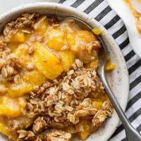 A bowl of peach crisp with a spoon in it.