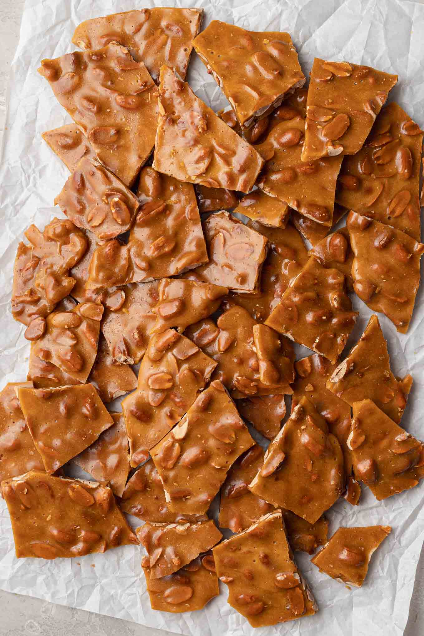 An overhead view of peanut brittle broken into pieces on a piece of parchment paper.