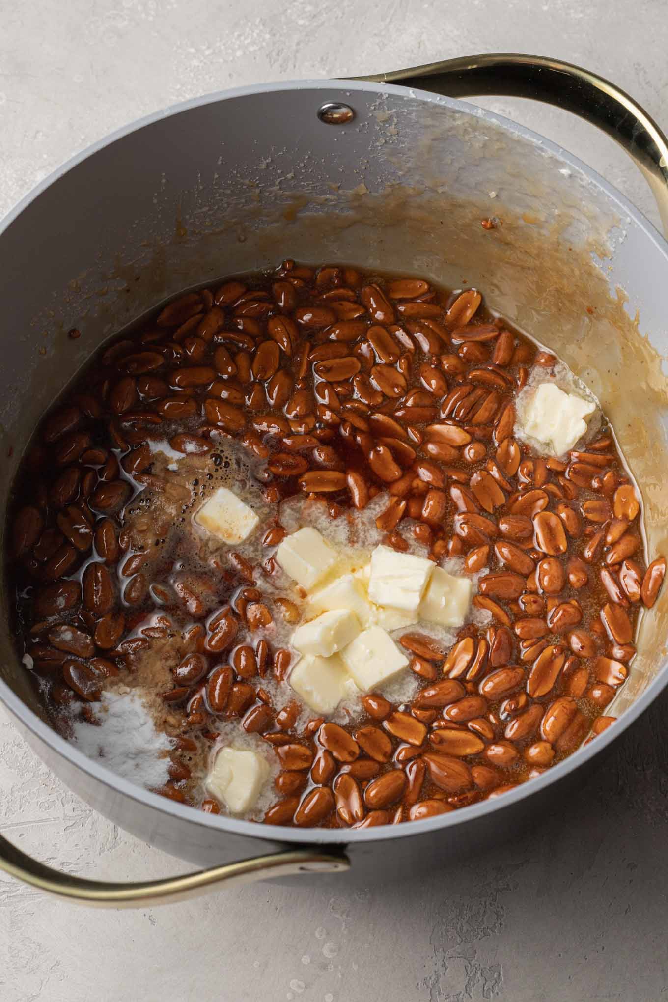 An overhead view of butter being added to a saucepan of peanut brittle. 