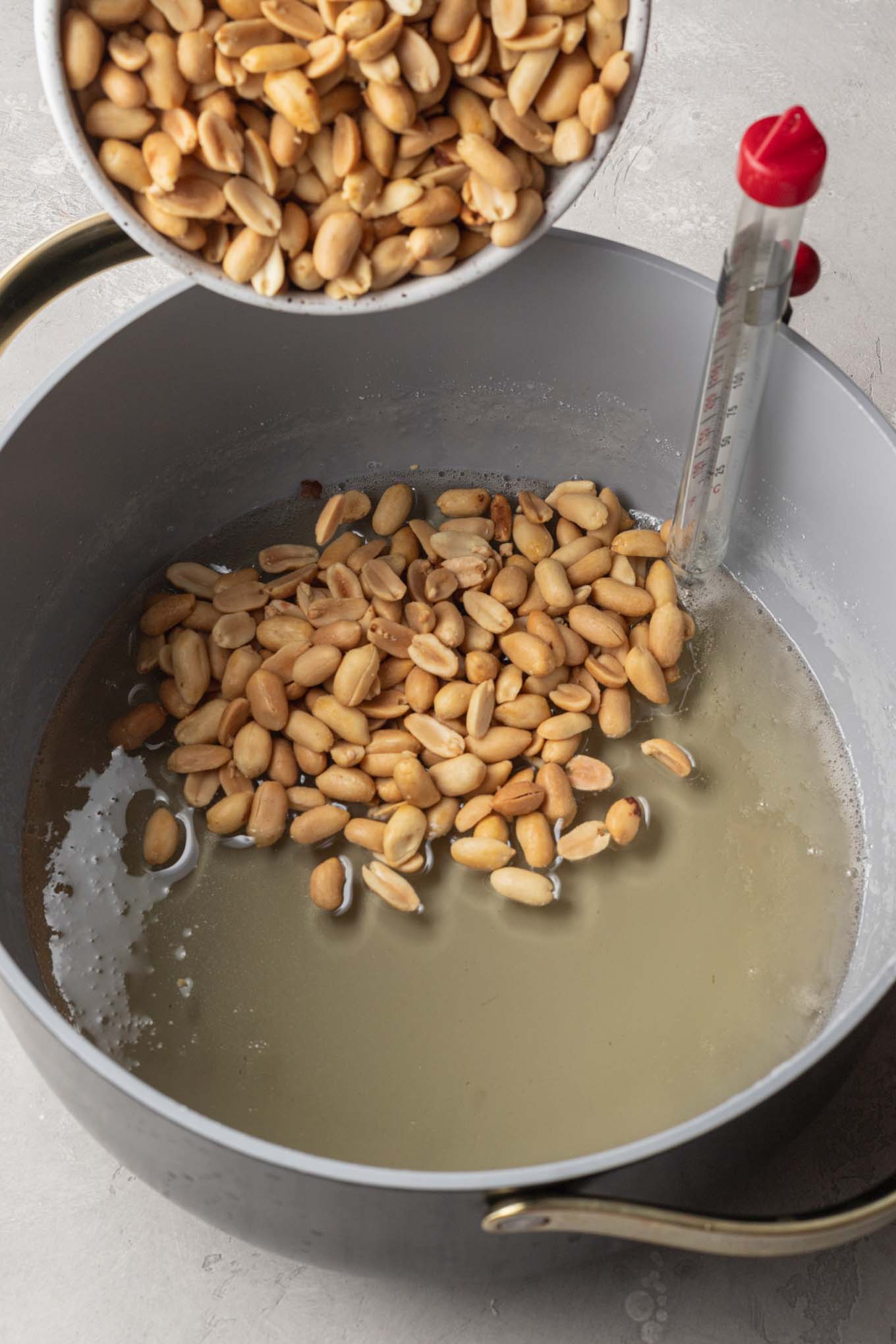 An overhead view of peanuts being mixed into a cooked brittle mixture in a saucepan. 