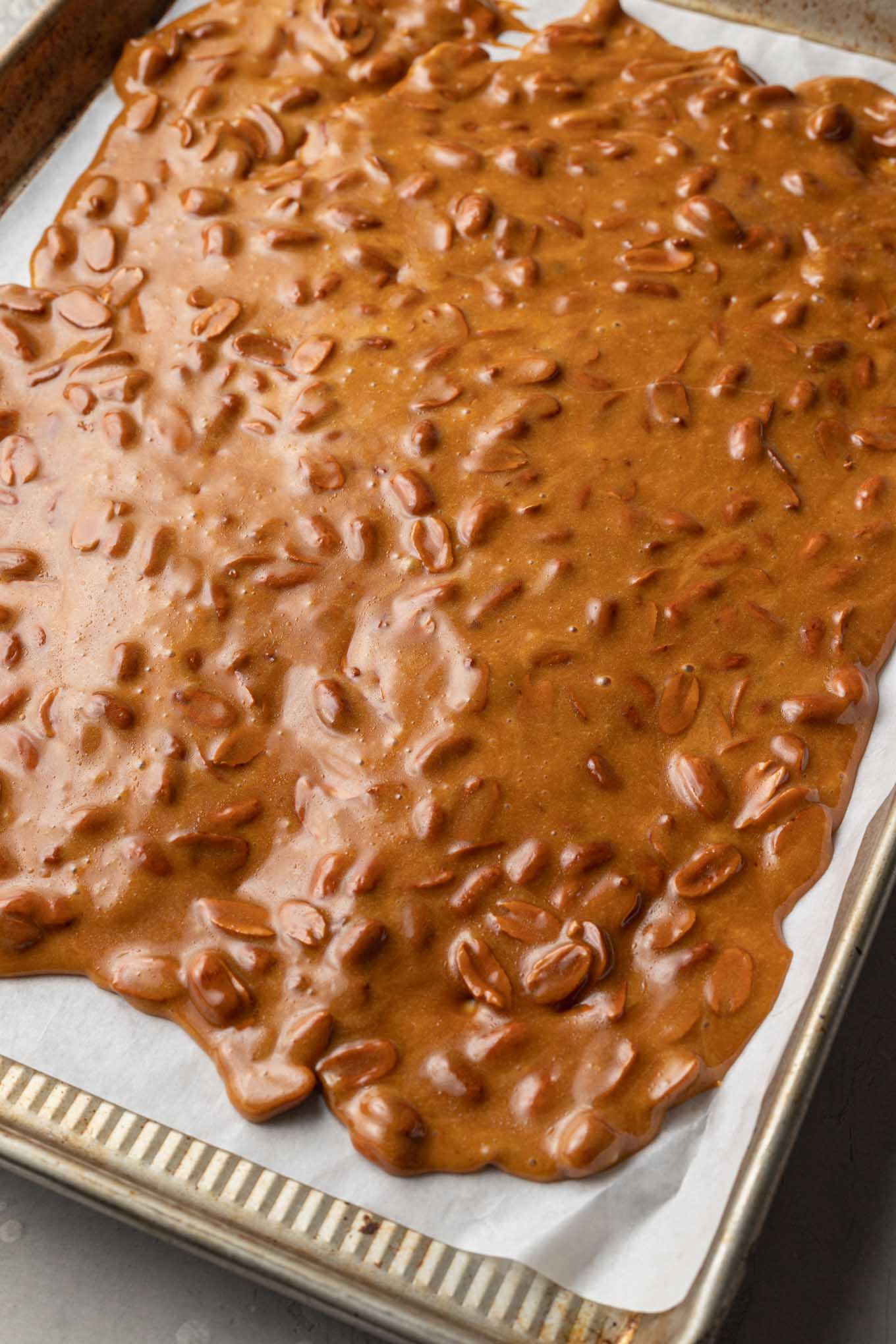 An overhead view of hot peanut brittle spread over a parchment paper-lined cookie sheet. 